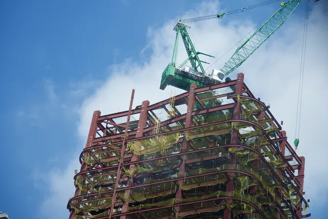 Rangka baja gedung bertingkat yang sedang dirakit dengan derek menara di atasnya
